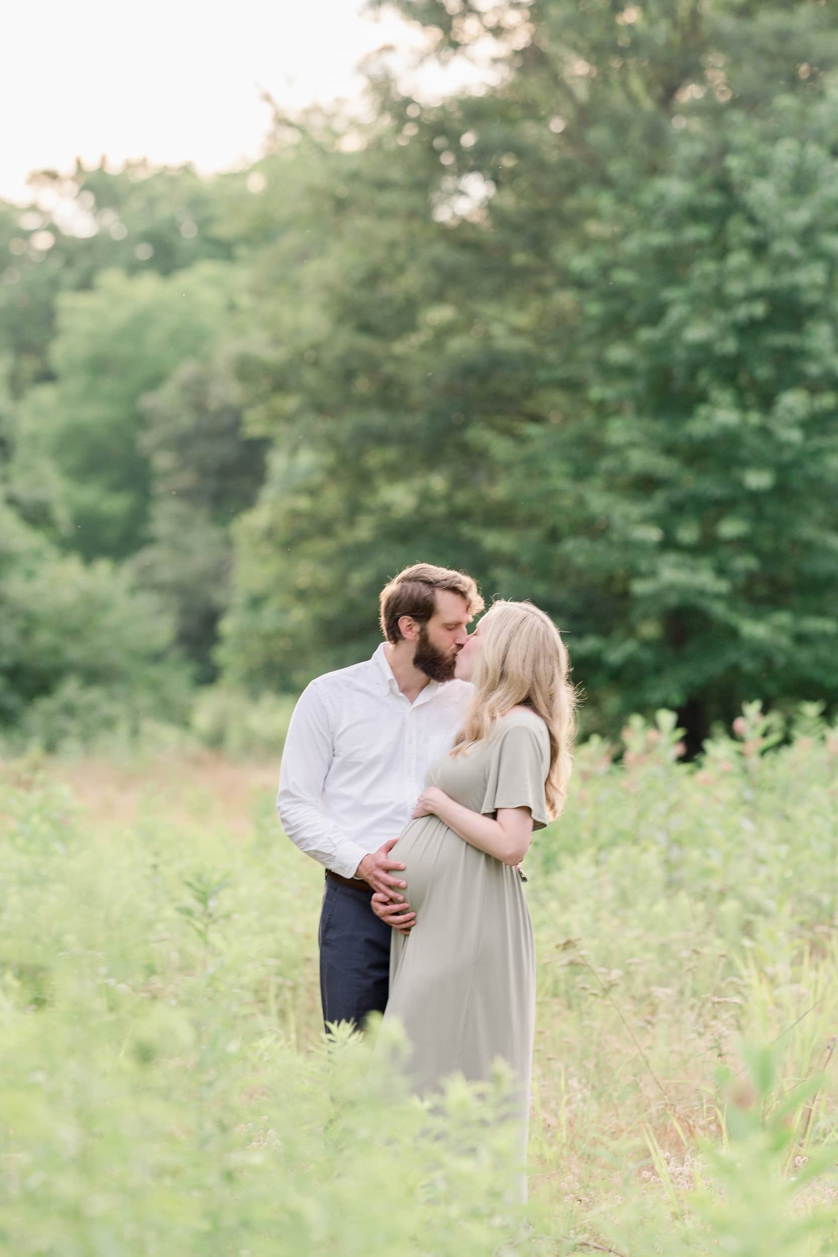 A pregnant couple kisses in a field by Moorestown Maternity Photographer Courtney Landrum.