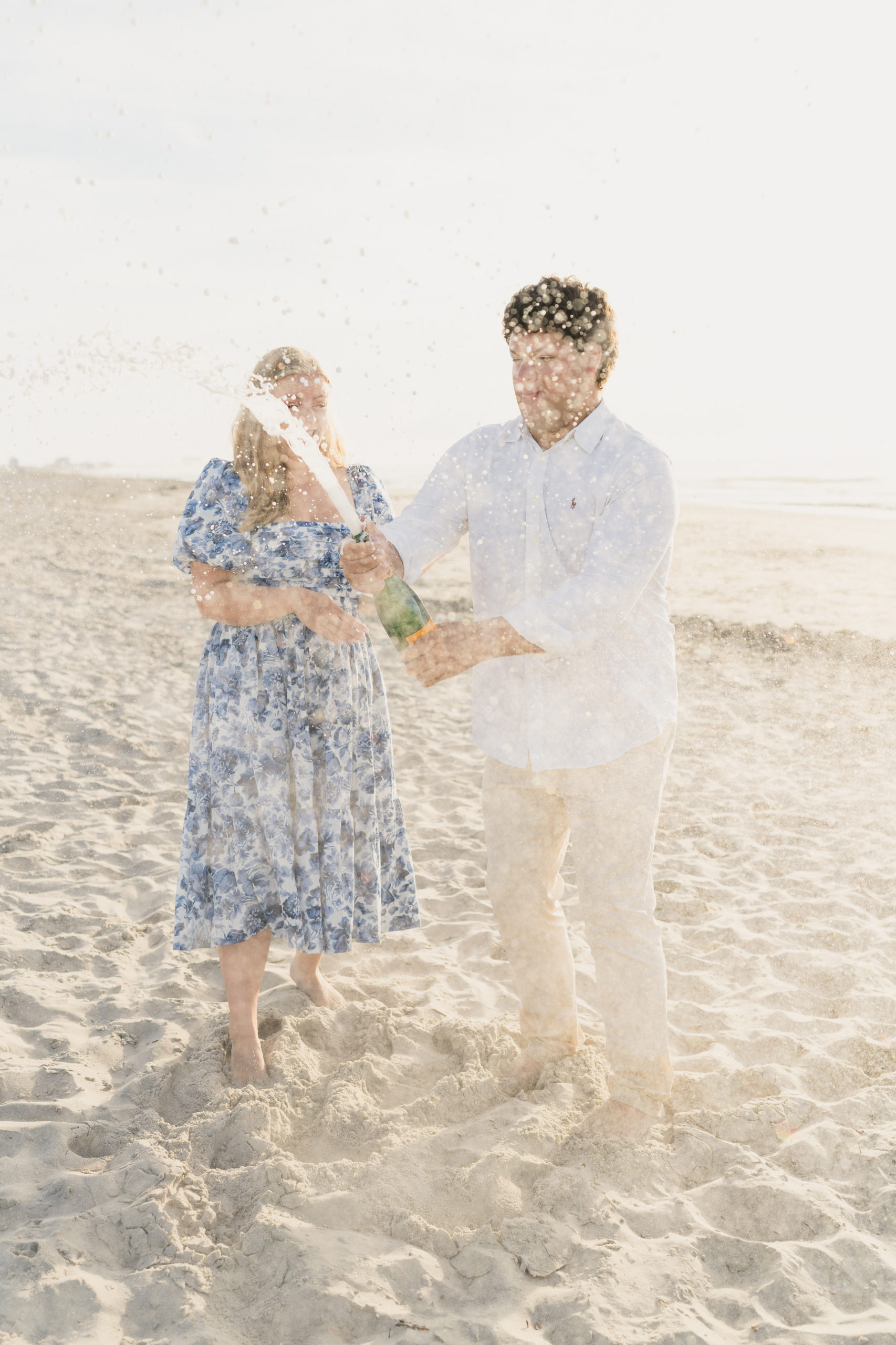 A couple sprays a champagne toast on the beach by Ocean City NJ Engagement Photographer Courtney Landrum.