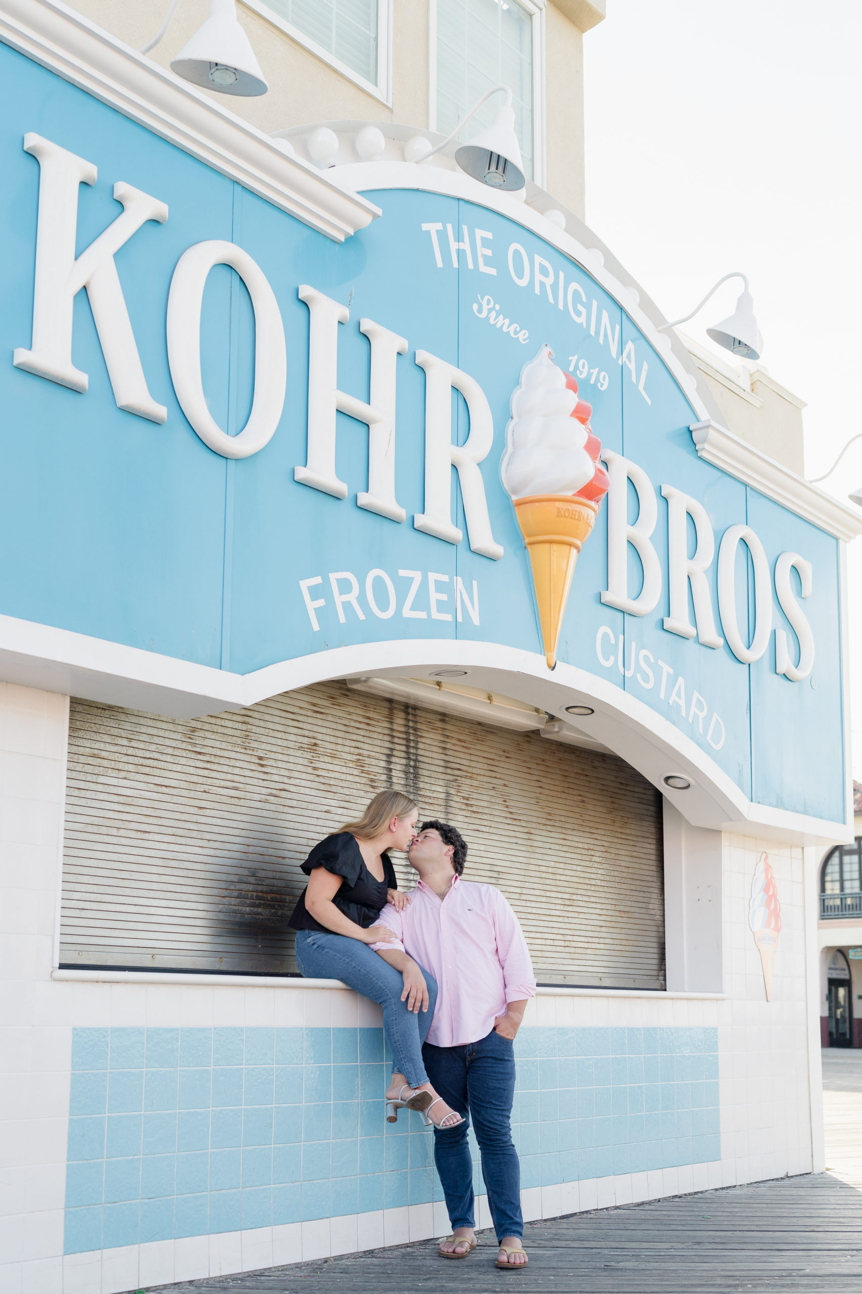 A couple kisses outside Kohr Bros by Ocean City NJ Engagement Photographer Courtney Landrum.