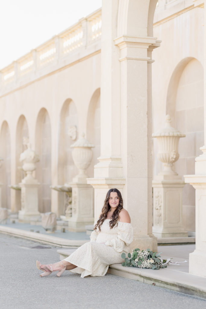 Pregnant woman sitting with a bouquet in front of beautiful Italian architecture.