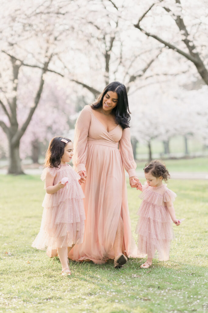 Mother wears a pink gown from Baltic Born while her daughters match in pink ruffly dresses.