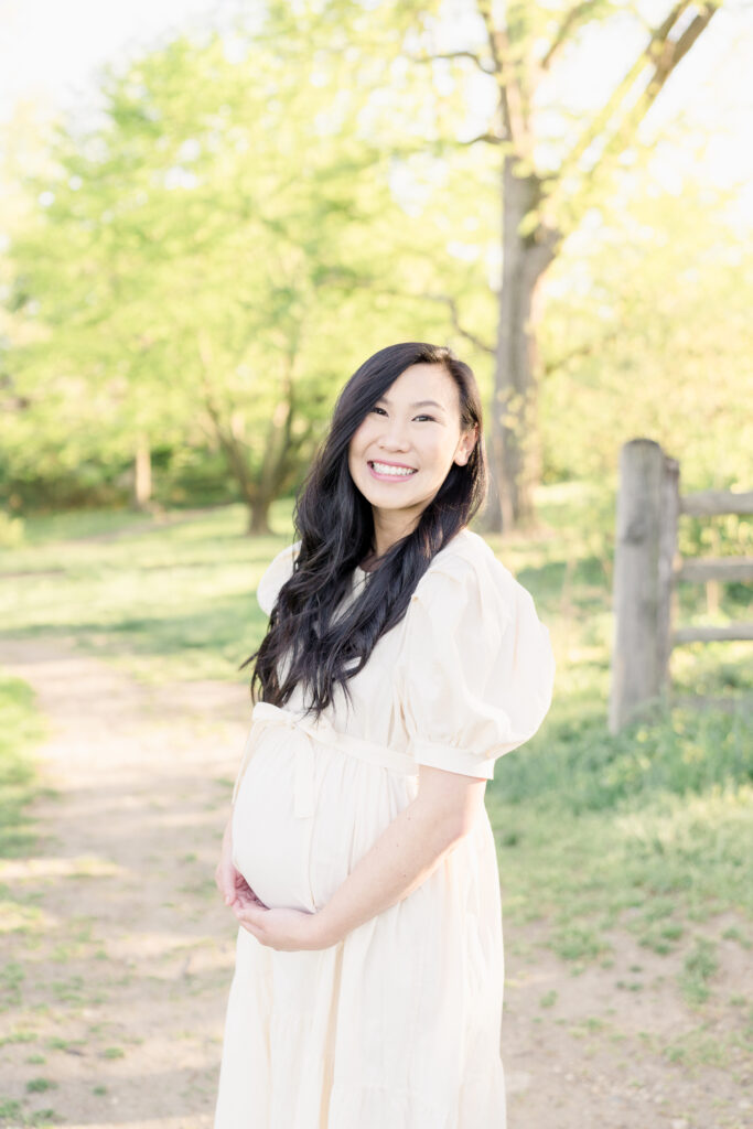 A pregnant woman holds her belly and smiles at the camera.
