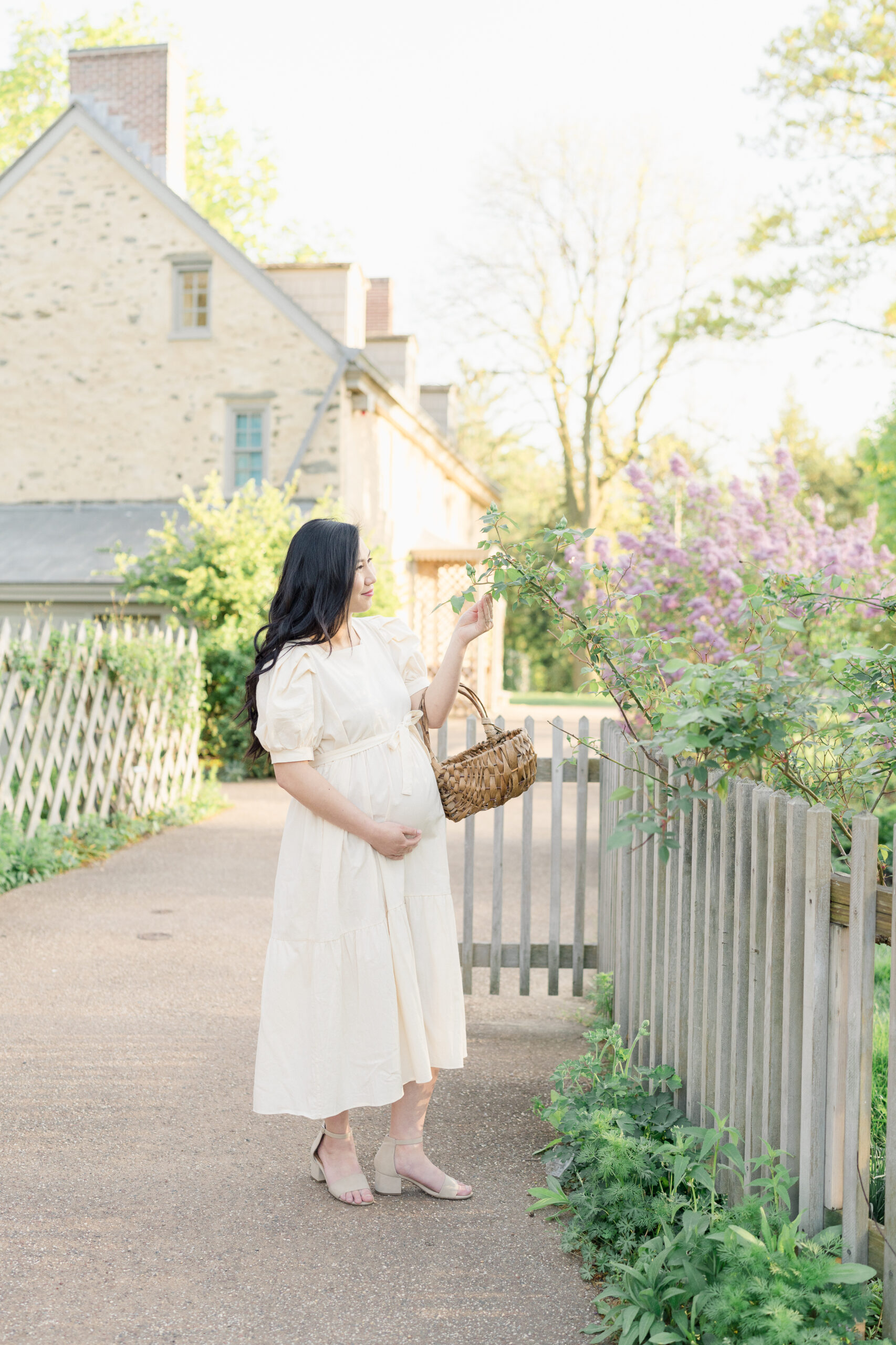 A mother expecting a little girl holds a gathering basket and is wearing a white dress for a whimsical pregnancy photoshoot.