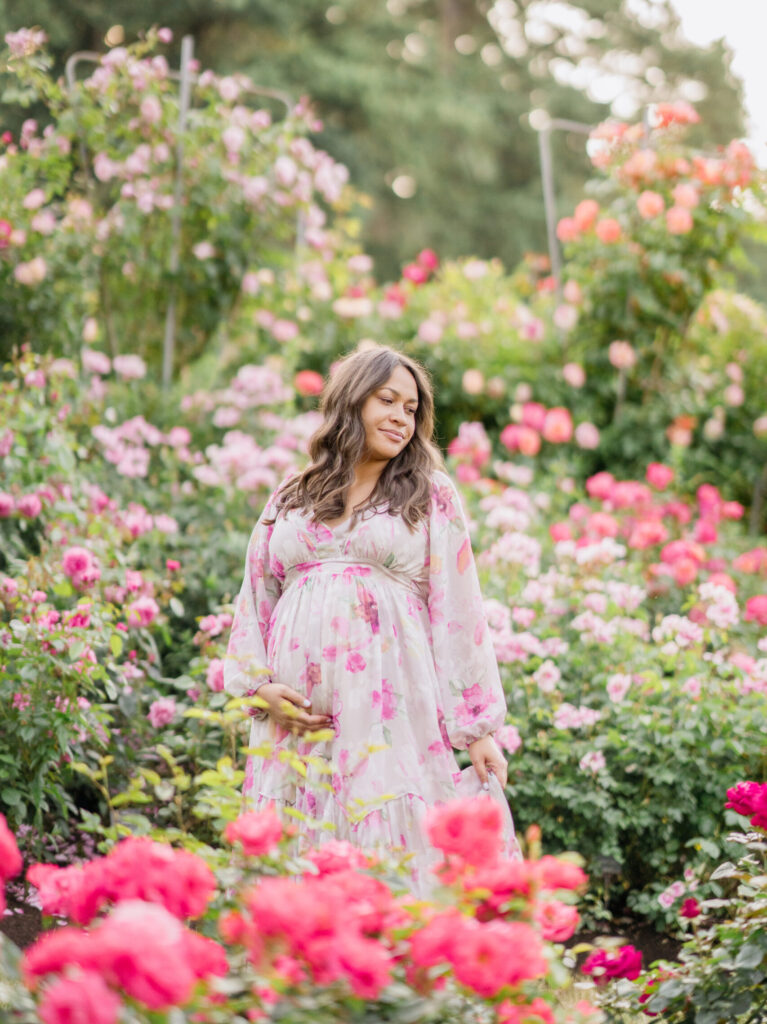 A woman stands in a garden full of roses for her first pregnancy announcement. 