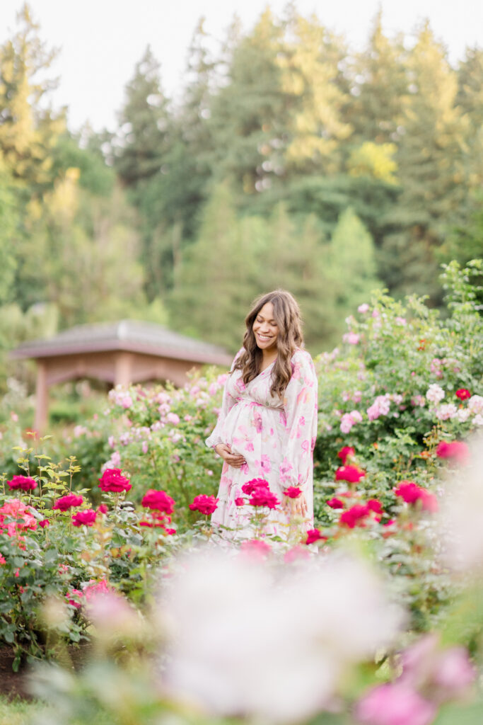 A mother expecting her first child stands in a rose garden and laughs.