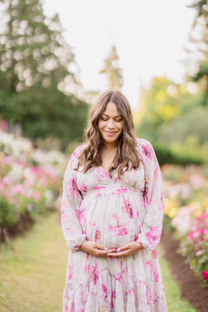 A pregnant woman at 22 weeks is wearing a floral dress and smiles down at her baby bump.