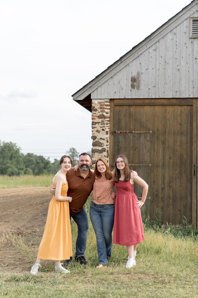 Family poses in front of rustic barn at Swedes Run park in Moorestown, NJ.