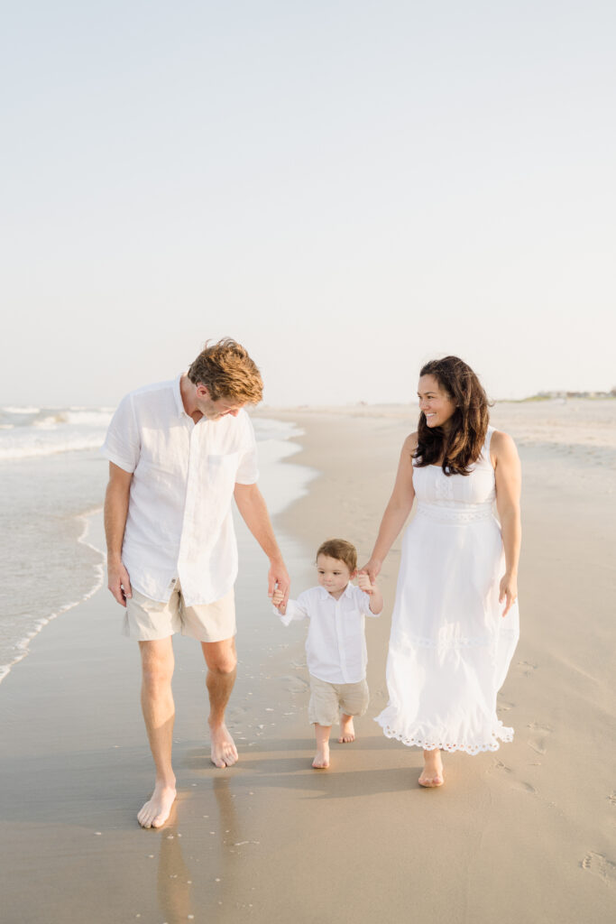 A family of three wears all white and walks along the surf at the Jersey shore.