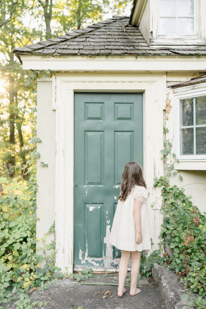 A little girl wearing a white dress tries to open a mysterious cottage door.
