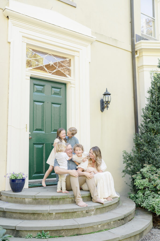 A mother, father, and their four children sit on the steps in front of a green door.