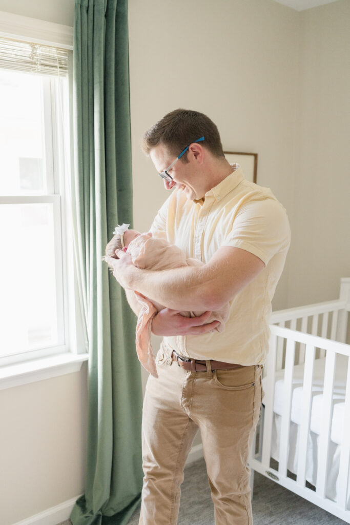 Dad holds his newborn baby girl wrapped in a peach muslin blanket.