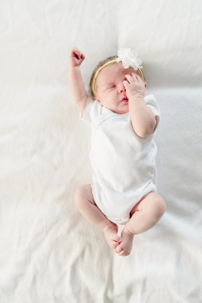 Newborn baby girl covers one eye and stretches.