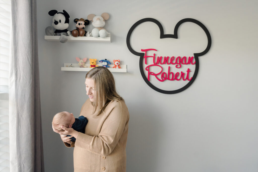 Mother holds her new baby in his Mickey Mouse themed nursery.
