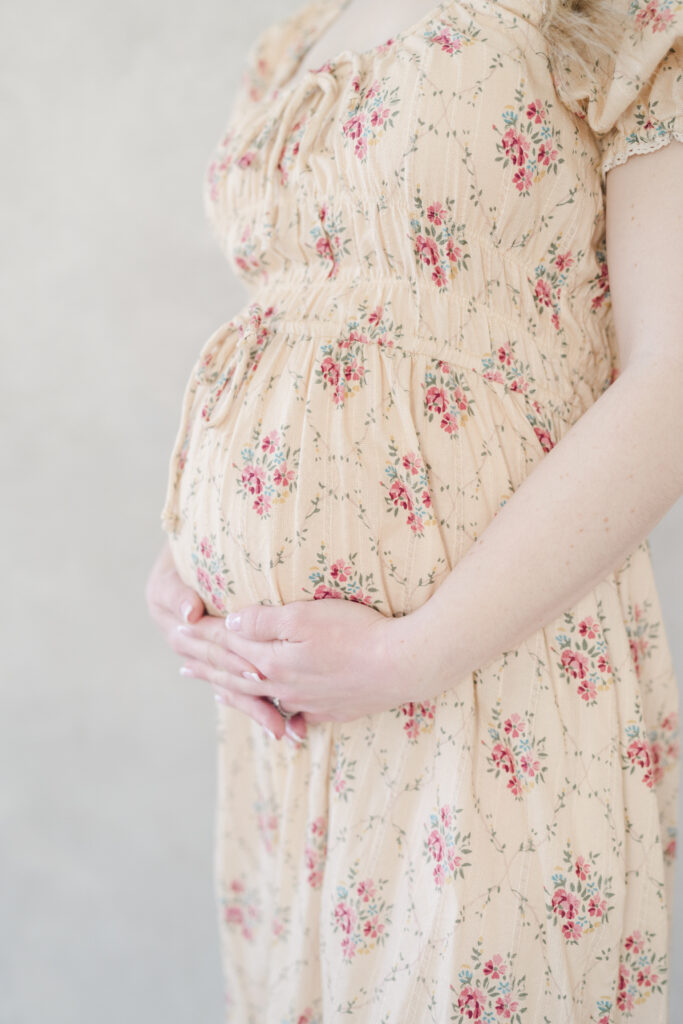 A pregnant mother holds her baby bump in a beautiful floral dress.