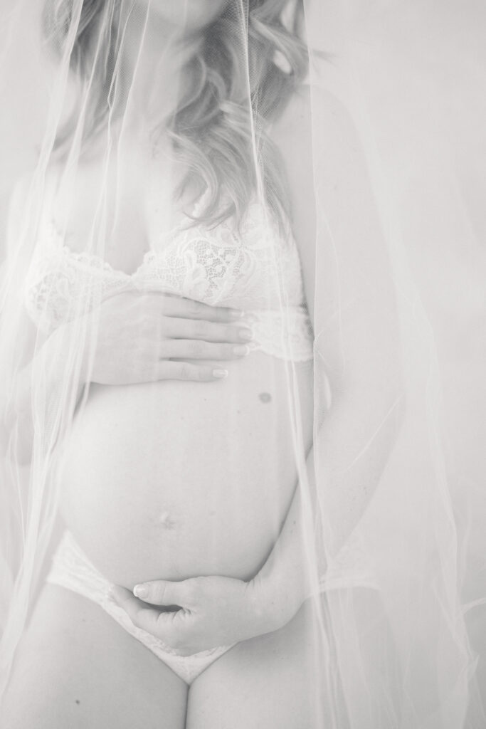 Black and white image of a bare baby bump covered in a veil.