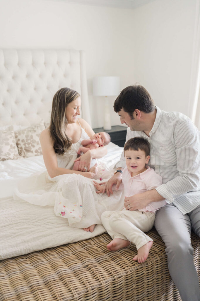Family of four relaxing on the bed with their newborn and toddler during a cozy photo session.