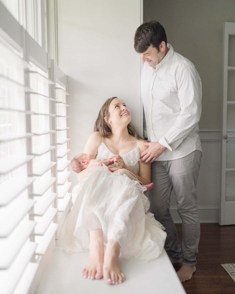 Mother holds her newborn baby snd sits in a window seat in her Haddonfield home.