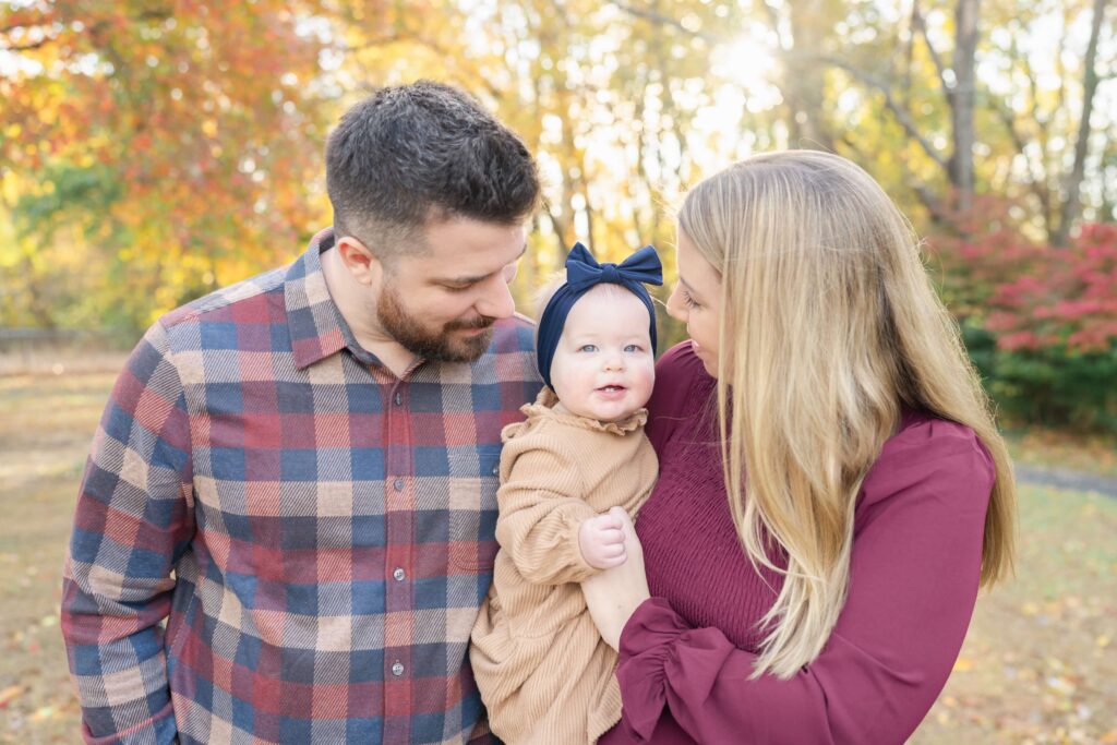 Parents cuddle their baby and smile in the fall leaves